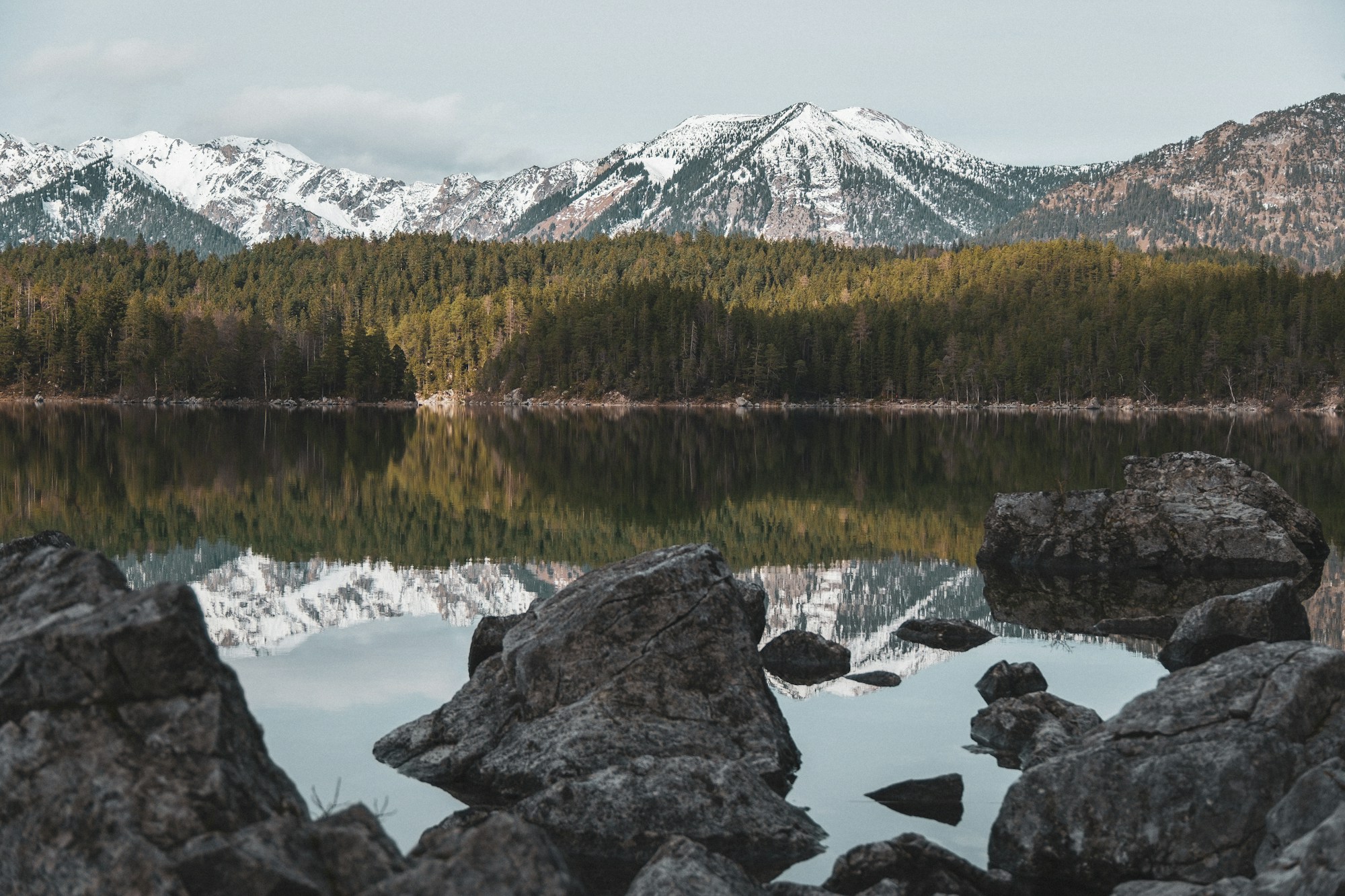Snow-covered Alpine peaks and a forested shore reflected in the still water of Lake Eibsee