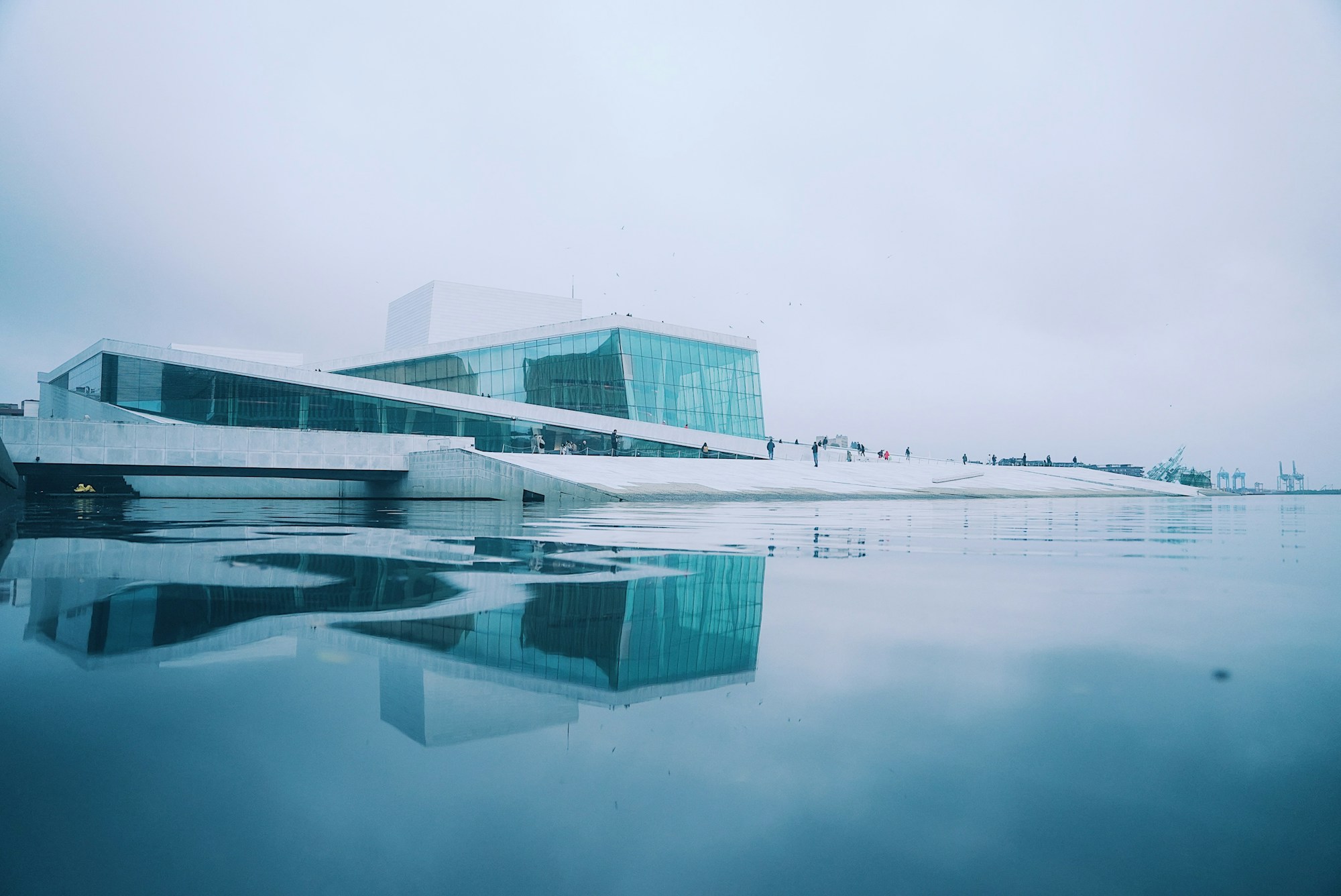The pale stone and glass of Oslo Opera House reflected in still blue water