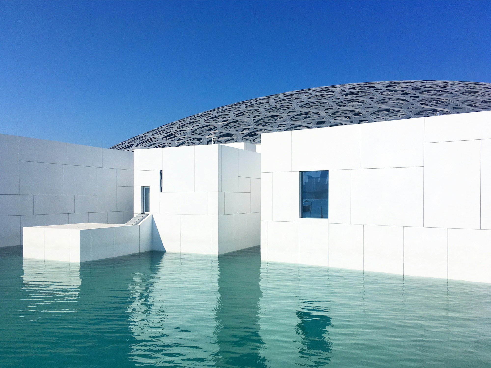 White walls and a patterned dome at Louvre Abu Dhabi above calm turquoise water
